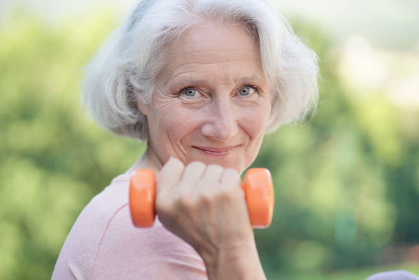 Portrait of smiling senior woman with white hair doing fitness exercises outside - Foto, afbeelding