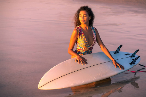 Portrait of woman surfer with beautiful body on the beach with surfboard at colorful sunset in Bali - Фото, зображення