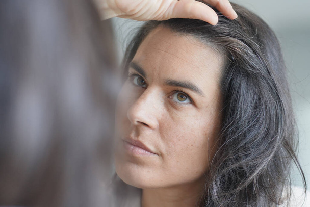 Middle-aged woman checking hair roots in front of mirror - Foto, Imagem