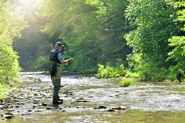 fly fisherman in summer fishing in a mountain river with waders and a cap - Foto, Imagen