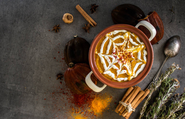 Spicy squash soup in ceramic pot. Halloween dinner top view photo. Dark grey background with copy space. - Photo, Image