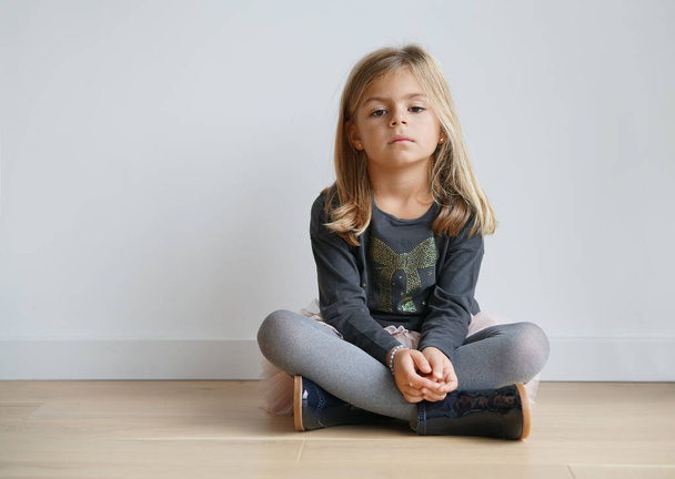 Cute little girl sitting on floor with serious look - Фото, изображение