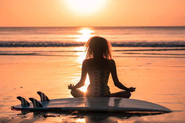 Portrait of woman surfer with beautiful body on the beach with surfboard at colorful sunset in Bali - Foto, afbeelding