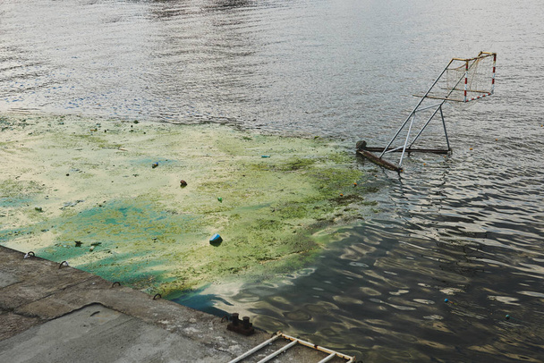 Kajak lub stadion water polo. Zanieczyszczenie wody zielonymi algami strunowymi, plastikowymi odpadami i innymi odpadami. Potrzeba czyszczenia wody. - Zdjęcie, obraz