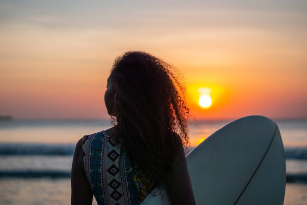 Porträt einer Surferin mit wunderschönem Körper am Strand mit Surfbrett bei farbenfrohem Sonnenuntergang auf Bali - Foto, Bild