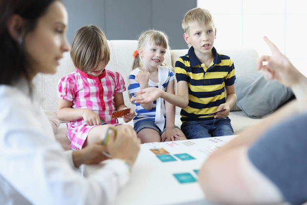 Volwassenen en kinderen zitten rond een tafel waarop speelkaarten liggen jongen discussieert en bespreekt de regels met een volwassene. - Foto, afbeelding