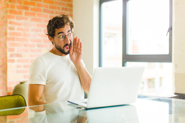young bearded man with a laptop profile view, looking happy and excited, shouting and calling to copy space on the side - Foto, Bild
