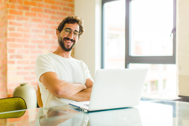 young bearded man with a laptop looking like a happy, proud and satisfied achiever smiling with arms crossed - Photo, Image