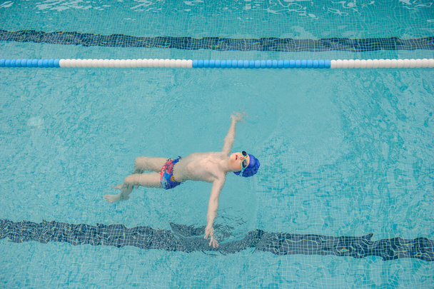 vista superior de un niño de 7 años nadando espalda en una piscina - Foto, Imagen