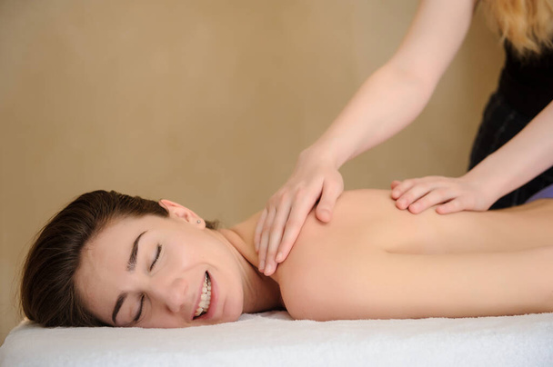visão lateral de uma jovem mulher recebendo uma massagem no pescoço e ombros feita por uma massagista em um salão de spa - Foto, Imagem