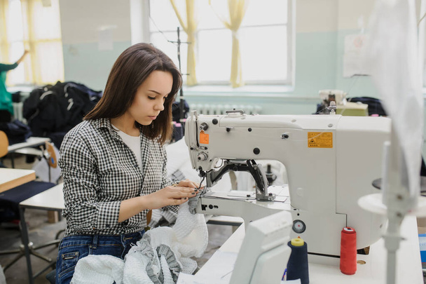 close up photo of a young woman sewing with sewing machine in a factory - Фото, зображення