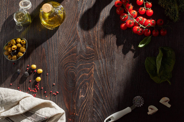 Вид сверху на темный деревянный стол со шпинатными листьями, помидорами, оливками, растительным маслом и специями. Шаблон для пищевой фотографии. - Фото, изображение