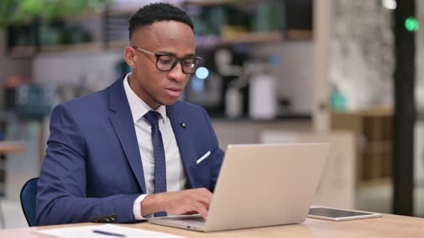 Fiatal afrikai üzletember laptoppal Mosolyog a kameránál az irodában  - Felvétel, videó