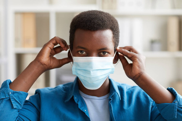 Голова и плечи портрет молодого афроамериканца, надевающего маску для лица во время работы в офисе после пандемии - Фото, изображение