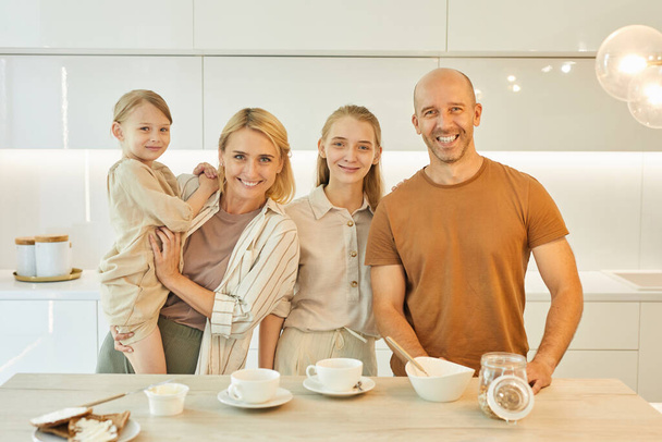 温かみのある腰をアップ現代の幸せな家族の肖像画をカメラを見て一緒に朝食を楽しみながら、最小限のキッチンインテリアでテーブルに立って、コピースペース - 写真・画像