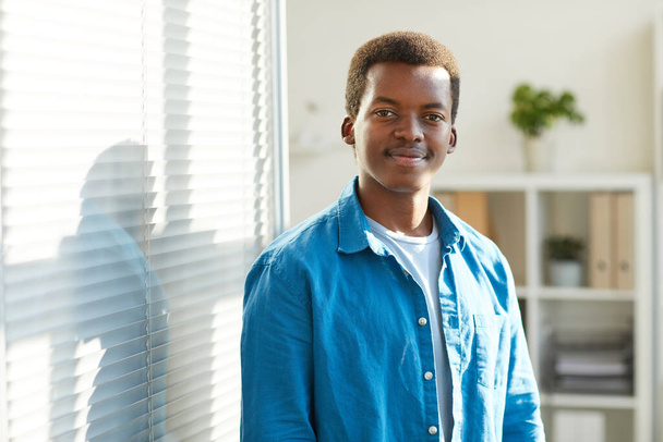 Vyötärö ylös muotokuva nuori afroamerikkalainen mies hymyilee kameralle seistessään kaihtimet toimistossa, kopioi tilaa - Valokuva, kuva