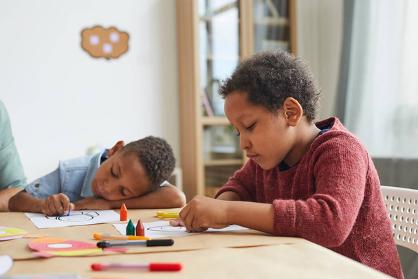 Retrato de vista lateral de niño afroamericano dibujando dibujos con lápices de colores mientras disfruta de clases de arte en preescolar, espacio para copiar - Foto, Imagen