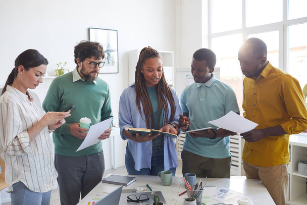 Portrait of contemporary multi-ethnic business team standing around table in office and listening to female African-American leader giving instructions, copy space - Photo, Image