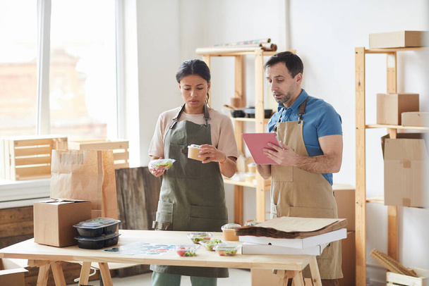 木製テーブル、食品配送サービス、コピースペースに立っている間にエプロン包装注文を身に着けている2人の労働者の腰の肖像画 - 写真・画像