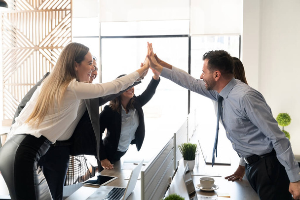 Business people standing around coworking desk in office and giving high five to each other - Photo, Image