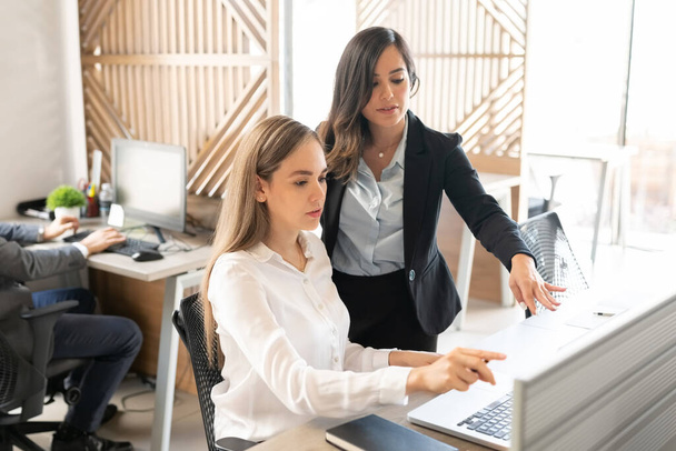 Επιχειρηματίας εξηγώντας θηλυκό συνάδελφο πάνω φορητό υπολογιστή στο γραφείο - Φωτογραφία, εικόνα