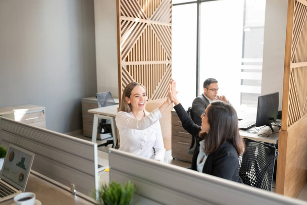 Happy business colleagues celebrating success and giving high-five while at office desk - Photo, Image