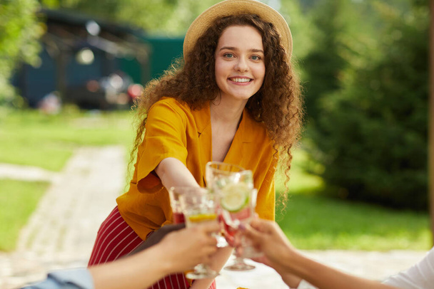 Waist up portrait of smiling young woman toasting with friends while enjoying dinner at outdoor terrace in Summer, copy space - Photo, Image