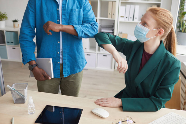 Portrait d'une jeune femme d'affaires portant un masque cognant les coudes avec un collègue comme salutation sans contact dans un bureau après une pandémie, espace de copie - Photo, image