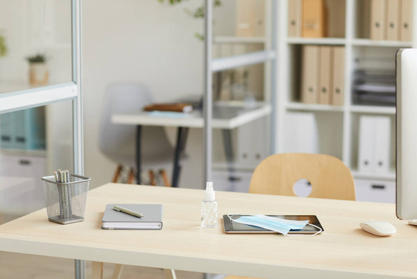 Háttérkép üres munkahelyi asztal arcmaszkkal és kézfertőtlenítővel a posztpandémiás irodában, másolás hely - Fotó, kép
