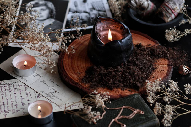 De spreuk over Samhain (Halloween) om contact te leggen met geesten van dode familieleden. Donkere en mysterieuze wicca heksenaltaar gevuld met vintage ansichtkaarten, foto 's, memorabilia, brandende kaarsen, vuil, zwarte aarde - Foto, afbeelding