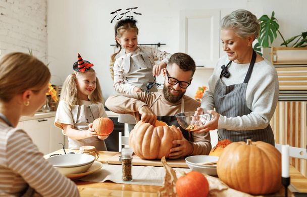 Szczęśliwi członkowie wielopokoleniowej rodziny z dyniami gromadzącymi się wokół stołu i przygotowującymi się do obchodów Halloween w kuchni w Hom - Zdjęcie, obraz