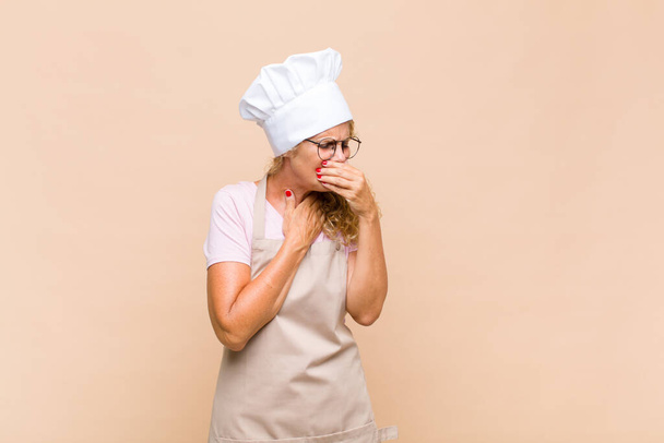 middle age woman baker feeling ill with a sore throat and flu symptoms, coughing with mouth covered - Fotoğraf, Görsel