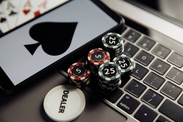 Online poker casino theme. Gambling chips, smartphone and playing cards on laptop keyboard - Photo, Image