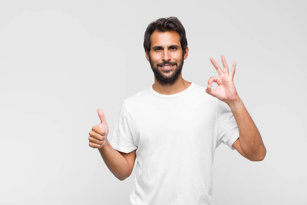 young latin handsome man feeling happy, amazed, satisfied and surprised, showing okay and thumbs up gestures, smiling - Photo, image