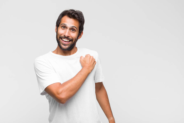 young latin handsome man feeling happy and smiling casually, looking to an object or concept held on the hand on the side - Fotoğraf, Görsel