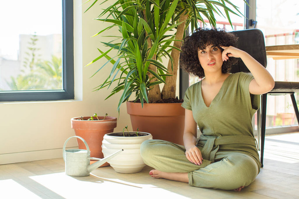 young pretty arab woman at home, with a watering can and plants - Foto, Imagen