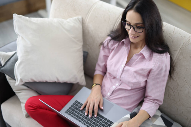 Женщина сидит на диване и работает на ноутбуке. - Фото, изображение