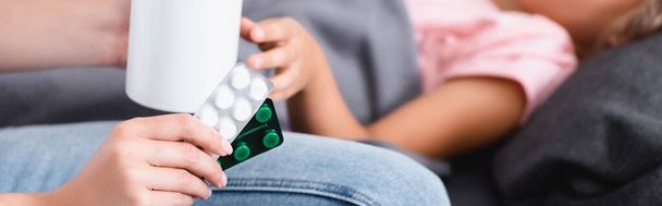 Cabeçalho do site da mulher segurando bolhas com pílulas e copo perto da criança em casa  - Foto, Imagem
