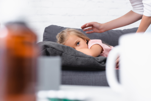 Selective focus of sick child looking at camera near mother on couch  - Foto, Bild