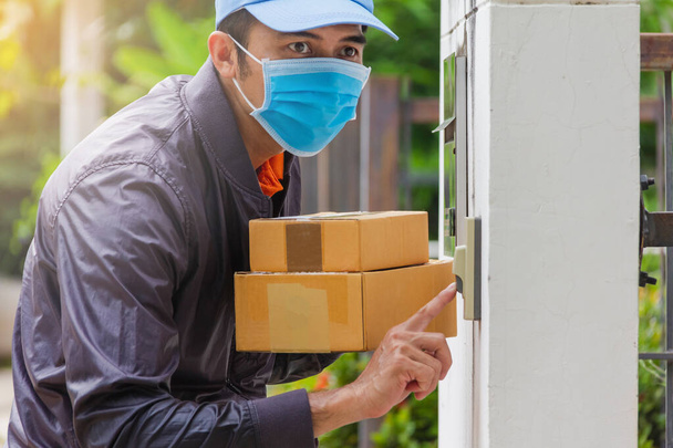 delivery man wear hygienic mask and blue cap pushing bell and holding cardboard box with look to customer for receive goods,light leak style - Photo, Image
