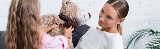Panoramic shot of girl giving teddy bear to mother at home  - Photo, Image