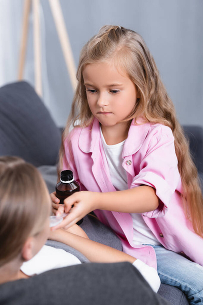 Selective focus of girl giving syrup to sick mother on sofa  - Foto, immagini