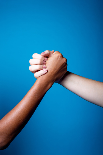 Schwarze und weiße Frauenhände, die einander Freundschaft und Respekt auf blauem Hintergrund zeigen - Vereinzelte multiethnische Frauenhände, die einander unterstützen - Brüderlichkeit, Rassismus, Gleichberechtigungskonzept - Foto, Bild