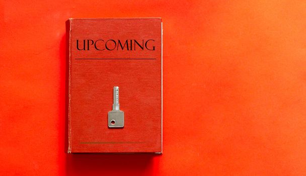 red book with text UPCOMING and a key on a red background - 写真・画像