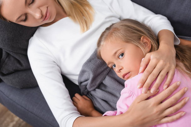 Top view of sick woman embracing child on couch  - Photo, image