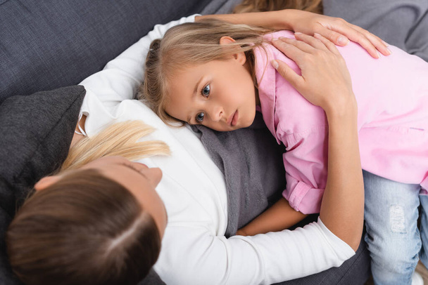 Yleisnäkymä sairas nainen syleilee tytär makaa sohvalla  - Valokuva, kuva