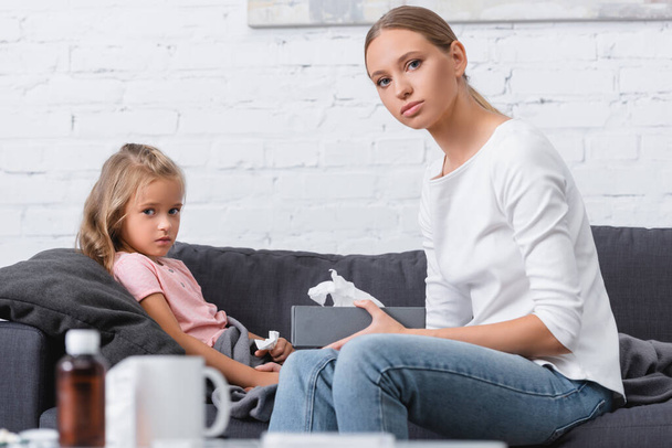 Enfoque selectivo de la mujer con servilletas al lado de la hija enferma en el sofá  - Foto, imagen