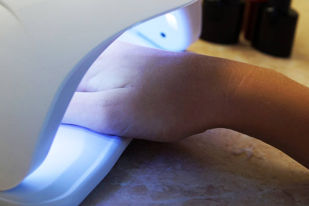 Çivi manikürü için ultraviyole lamba takan kadın eli. - Fotoğraf, Görsel