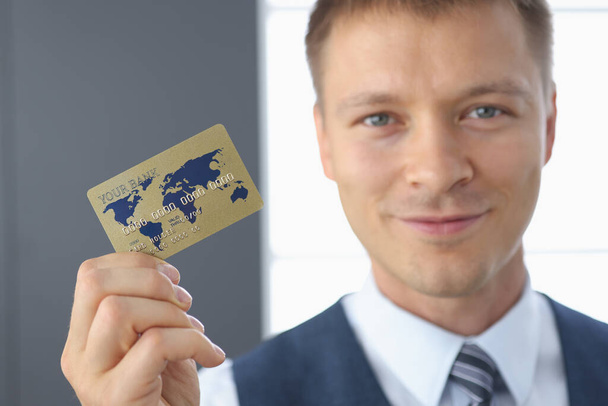 Un hombre de negocios sonriente tiene una tarjeta de banco de plástico en su mano - Foto, Imagen