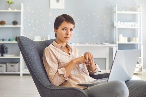 Serious businesswoman sitting in comfortable armchair with laptop in cozy home office - Fotografie, Obrázek
